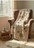 Floral quilt draped over a brown armchair next to a window with a cup and books on a small table.