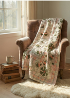 Floral quilt draped over a brown armchair next to a window with a cup and books on a small table.