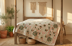 Bed with a floral quilt in a sunlit bedroom with plants and macrame art.