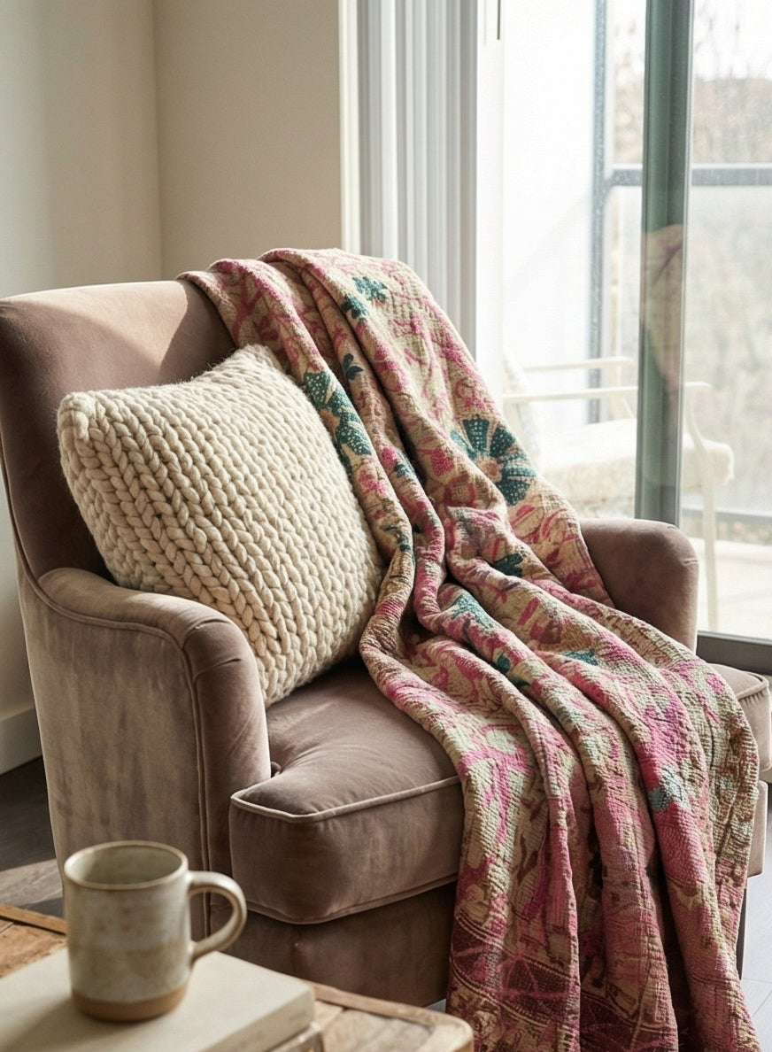 Cozy living room scene with a brown armchair, patterned blanket, and textured pillow.