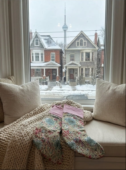 Decorative stockings on a staircase, table, and window seat with a snowy view.