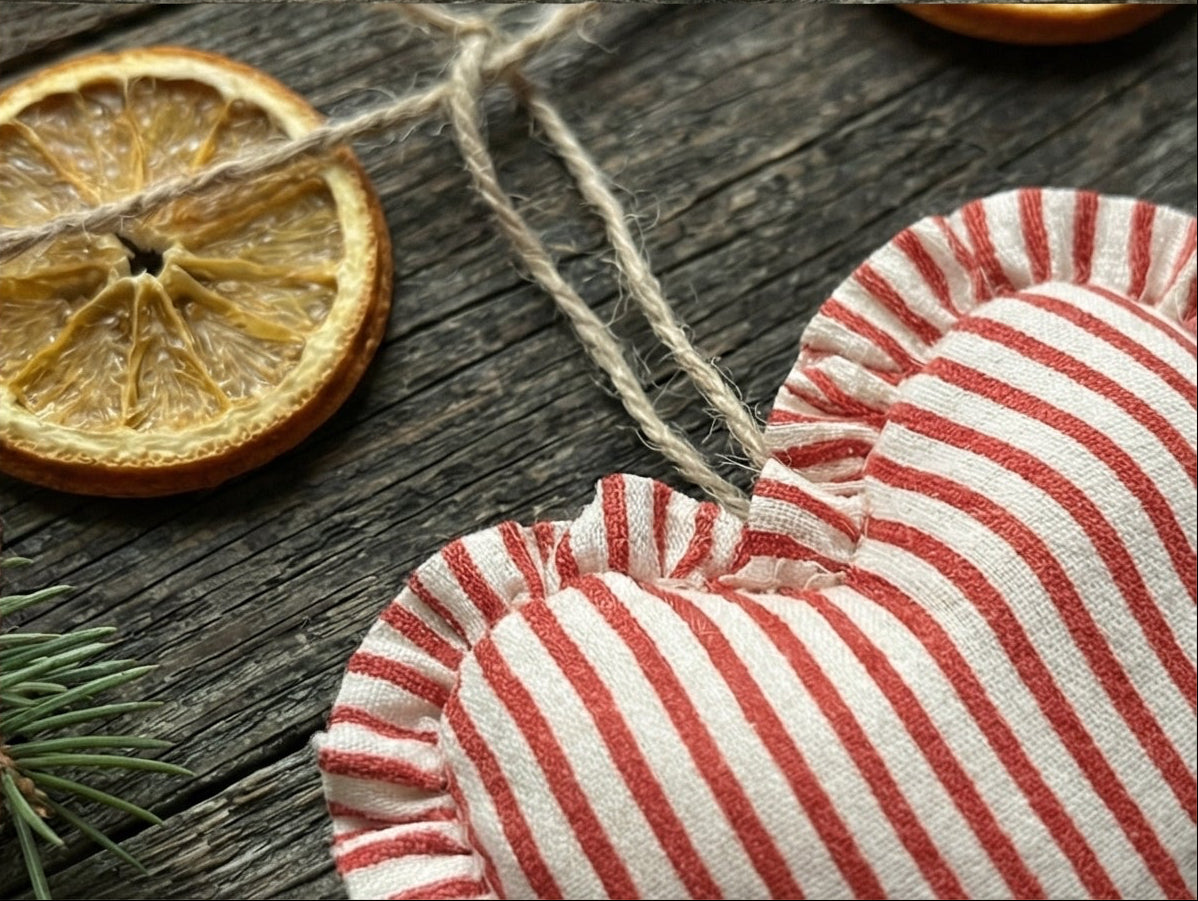 Red and white striped heart-shaped fabric on a wooden surface with a dried orange slice and twine.