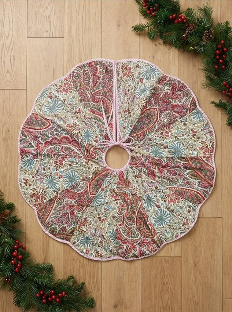 Patterned Christmas tree skirt and tablecloth on a wooden floor with a decorated tree and fireplace.