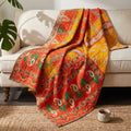 The Nomad Trail Vintage Cotton Kantha Throw showcases a rich design in orange, yellow, green, and cream, featuring paisley motifs, stylized bird patterns, floral designs, and geometric borders.