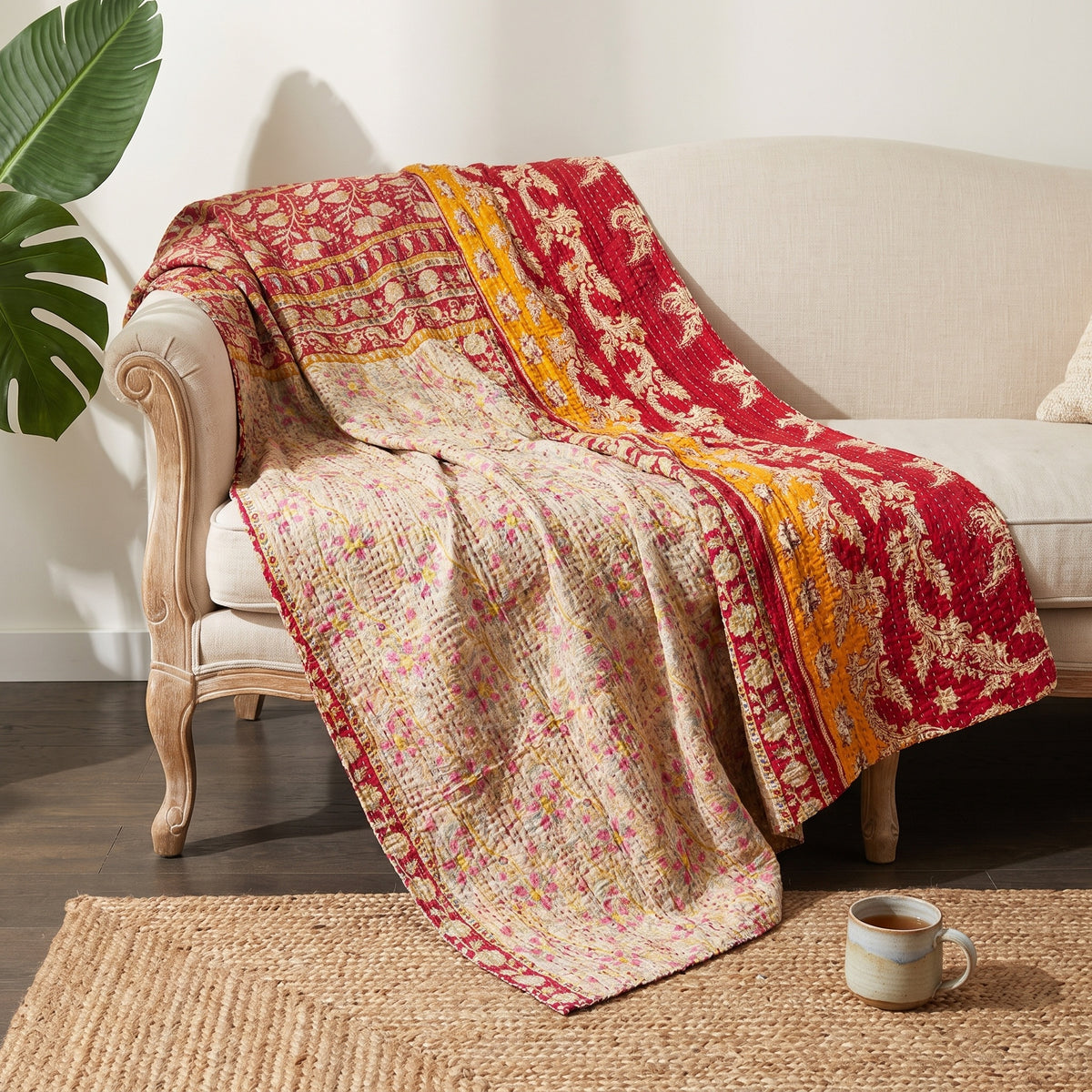The Wanderer's Tale Vintage Cotton Kantha Throw showcases deep red, mustard yellow, cream, and pink hues, intricately patterned with large floral and vine motifs, small scattered flowers, and striped borders.