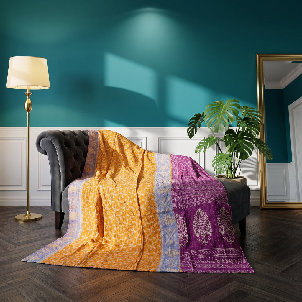 A Quiet Passage Vintage Cotton Kantha Throw featuring saffron yellow with small abstract geometric patterns, a periwinkle blue strip with faint abstract patterns, and a royal purple section with large floral medallions and geometric borders, draped over a dark grey sofa.